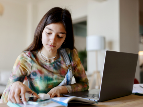 A female teenager sits in her room on her computer. She is in Charlie Health's virtual IOP and knows the risk factors for suicidal thoughts and outcomes at Charlie Health.