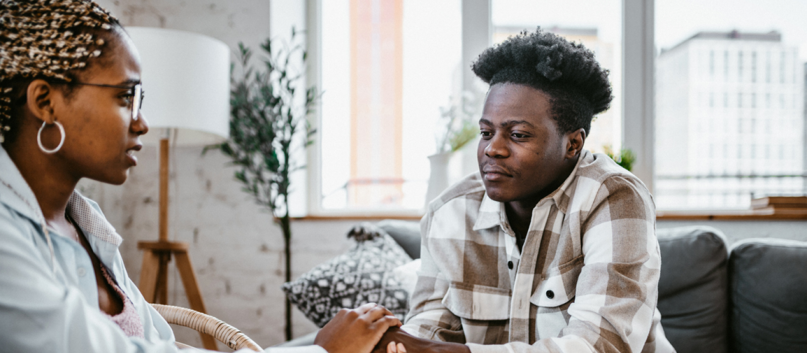 A young woman and man sit on their couch holding hands. The woman is checking in on her friend who has been having subtle signs of depression.