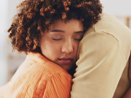 A young woman in an orange sweater hugs her partner in a yellow shirt. She is dating someone with depression and uses tips to help her partner.