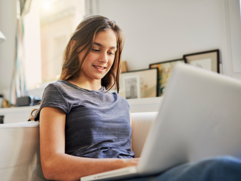 A teenage female sits on her couch at home on her computer. She is in Charlie Health's virtual IOP.