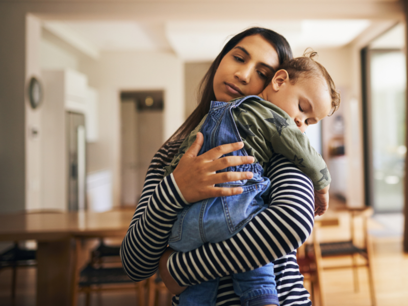 A young mom is holding her child and comforting them. She is experiencing mom burnout and is learning how to deal with it.