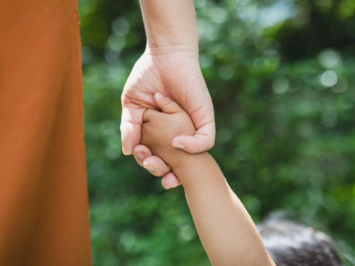 A young mother holds her childs hand. She has postpartum depression and could benefit from a program like Charlie Health.