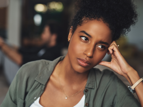 A young woman sits on the couch looking upset. She has experienced emotional abuse that has caused trauma and she is learning how to heal.