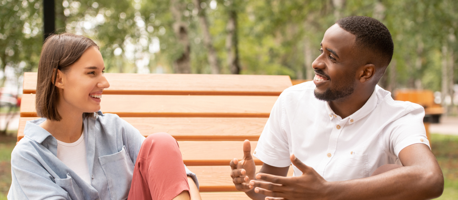 A woman and a man sit on a park bench. The male has attachment issues and he is talking to his good friend that he has a healthy relationship with.