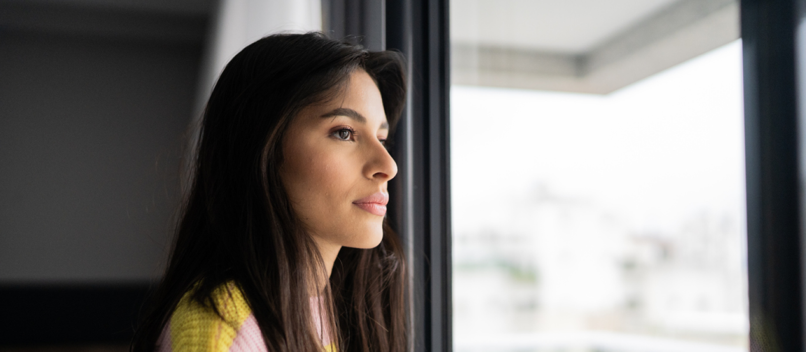 A young woman looks out her window. She is having self-esteem and identity issues due to an emotionally abusive parent.