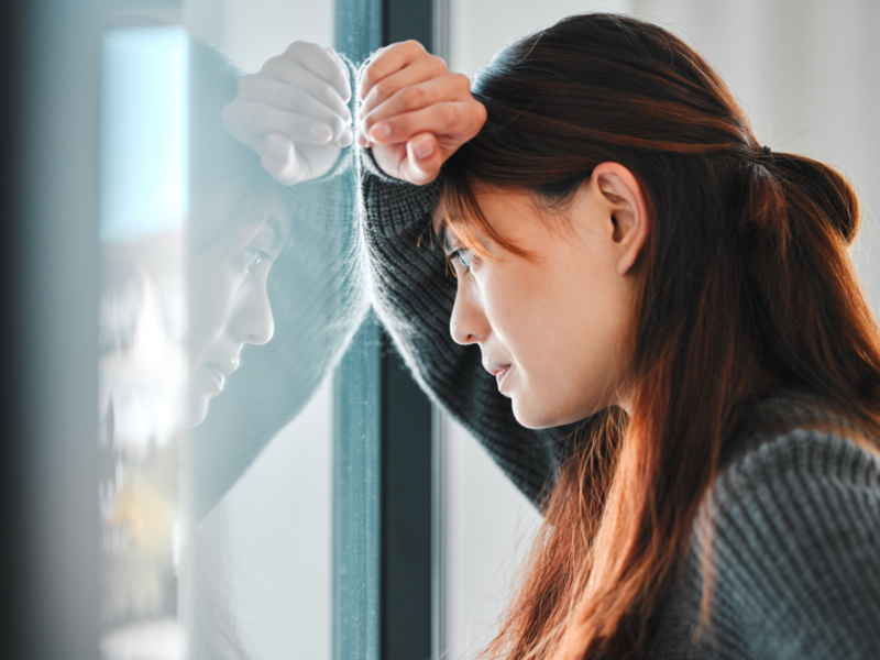 A woman stares out the window upset. She has abandonment trauma and thinks that may be why relationships stress her out.