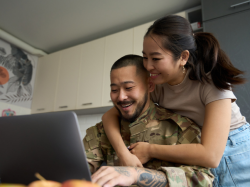 A male in the military sits at his computer with his wife. They are a military family and want to learn more about personalized care at Charlie Health.