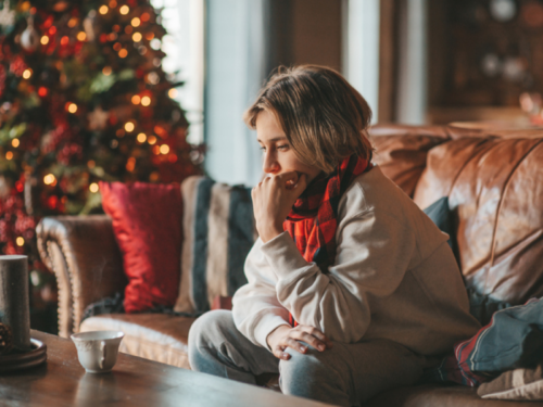 A young woman sits at home alone during the holidays. She needs 5 therapist-approved tips for holiday loneliness to use year-round.