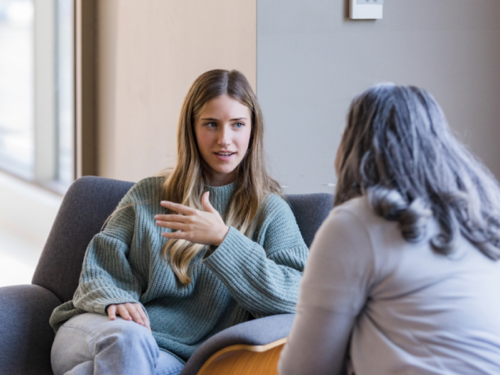 A mother sits with her daughter on a couch. The daughter has paranoid delusions, and the mother is figuring out what to say (and not say) to her that can display empathy and support.