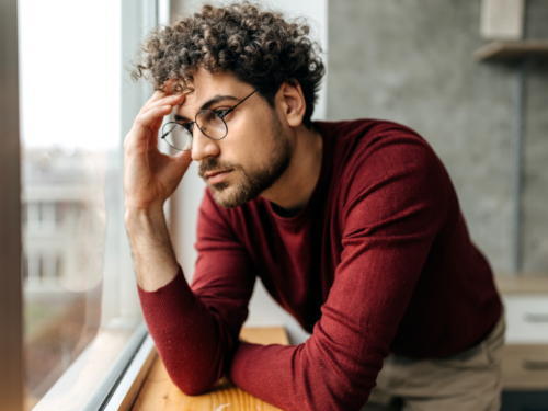 A young man looks out of his window upset. He wants to fix his attachment issues and us using therapist-approved tips to do this.