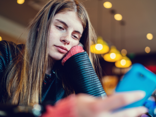 A young girl sits on her phone at the store. She feels like she has no motivation all of the time.