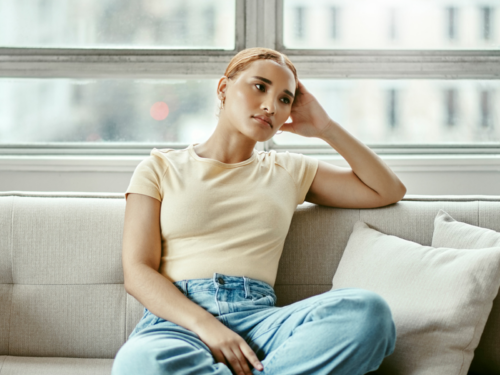A young woman sits on her couch, frustrated. She doesn't know if she is doing the silent treatment or has passive-aggressive personality disorder.