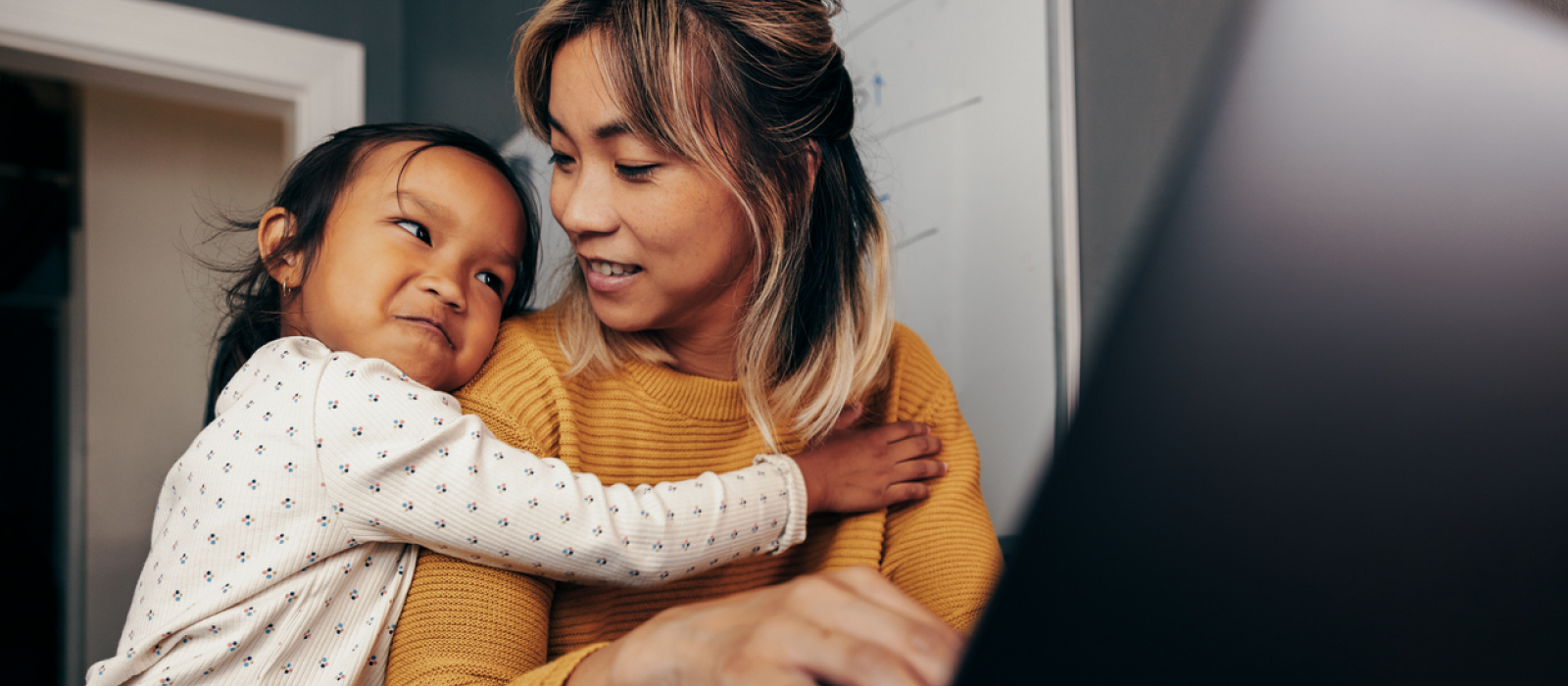 A young mother and her child are at home. The mother is logging on for mental healthcare that is accessible to her via telehealth.