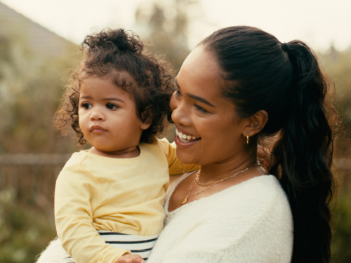 A young mother smiles with her child. She is learning how Charlie Health is addressing the maternal mental health crisis.