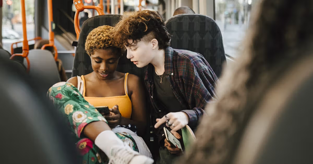 Teen showing something on her phone to her friend on the bus