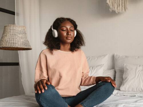 A person wearing headphones sits with her legs crossed while listening to a meditation for depression.