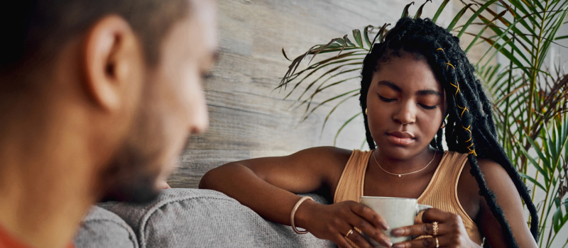 A person with high-functioning anxiety wearing a tank top sits on a couch drinking tea.