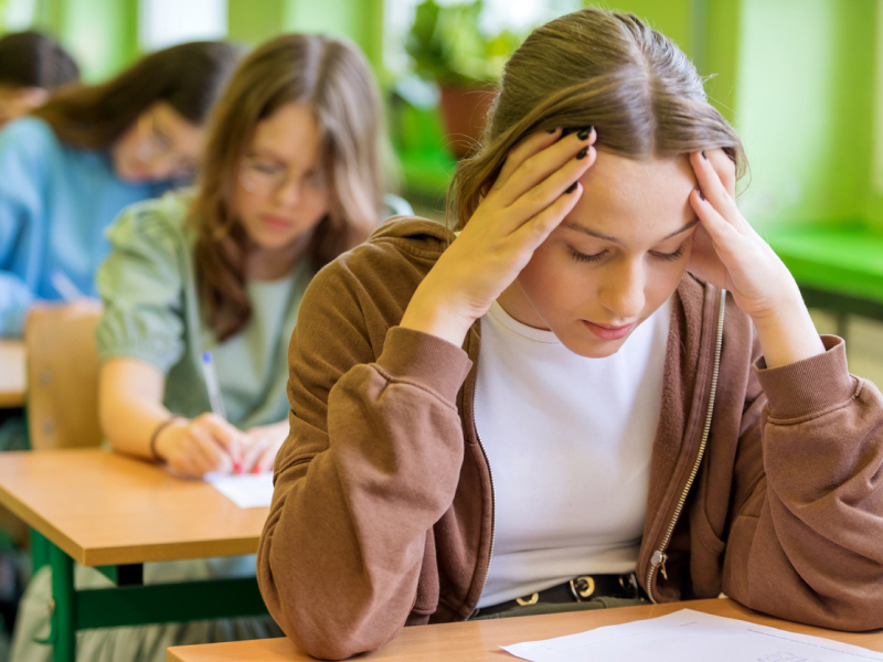 A person with high-functioning anxiety sits at school holding her head.