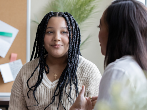 A woman wearing a white sweater sits on a couch talking with a therapist about how to use DBT for PTSD.