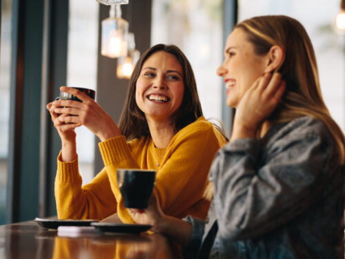 Two women sit next to each other drinking coffee and smiling after attending group therapy for postpartum depression.