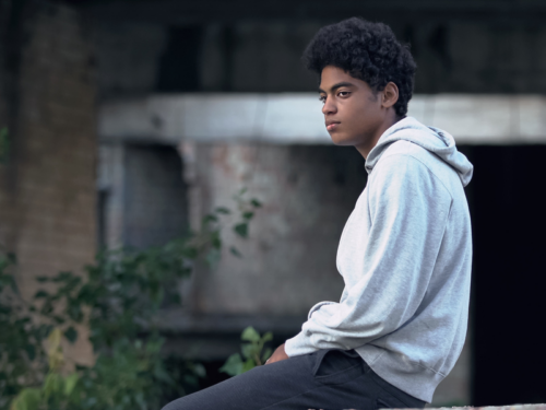 A boy in a sweatshirt sits on a fence using a DBT skill to help him manage schizophrenia.