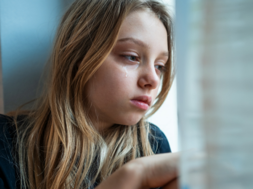 A young girl looks out a window in grief. She could use DBT to cope with grief.