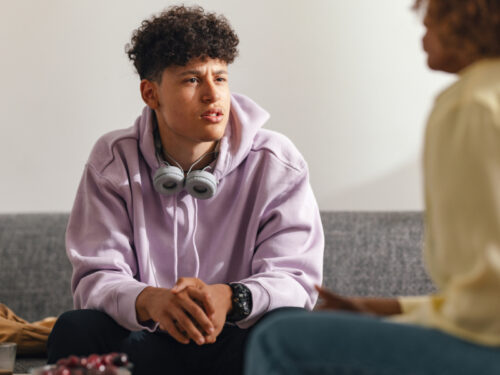 A boy in a purple hoodie sits in a group therapy for ADHD session with a counselor.