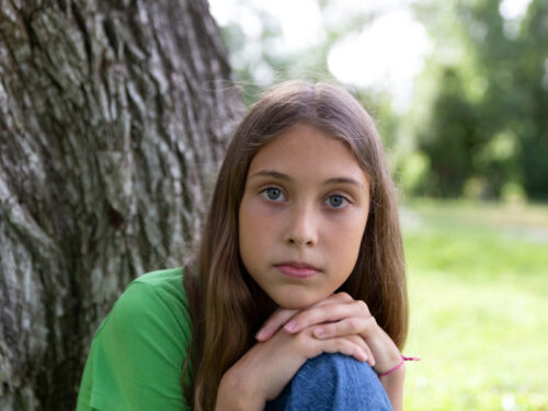 A girl struggling with self-esteem sits in front of a tree thinking about group therapy for self-esteem.