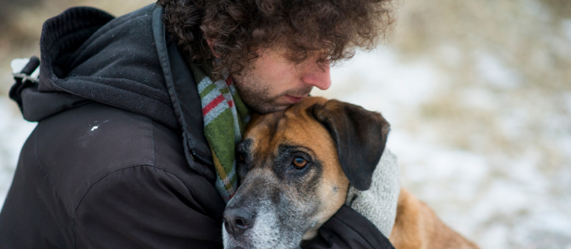 A person in a jacket hugs their pet (a big dog).