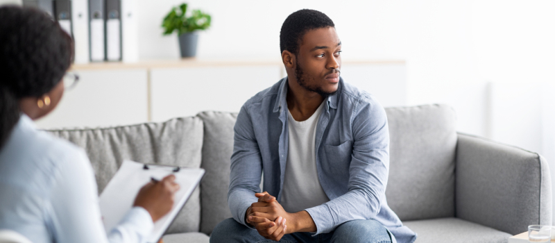 A person sits on a grey couch in a therapist's office answering C-SSRS questions.