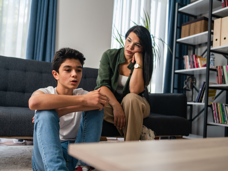 A person sits on the ground next to his mom on a couch as he contemplates the effects of growing up with a bipolar parent.