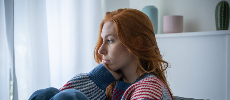 A woman with orange hair sits and stares into the difference as she struggles with false memory OCD.