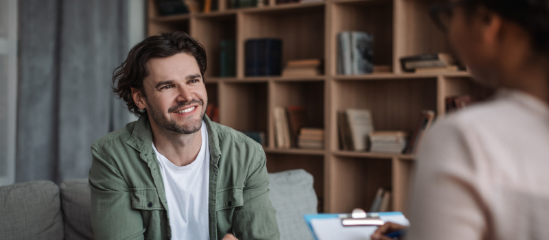 A man in a green shirt sits in a therapy session smiling as he learns about the DBT wise mind skill.