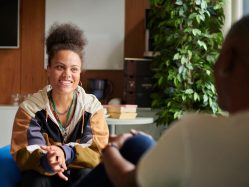 A woman in a jacket sits in a therapy session smiling. She is using therapy and medication for bipolar disorder.