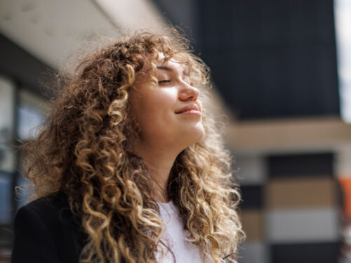 A woman with curly hair sits in the sun smiling after using her DBT wise mind skill.