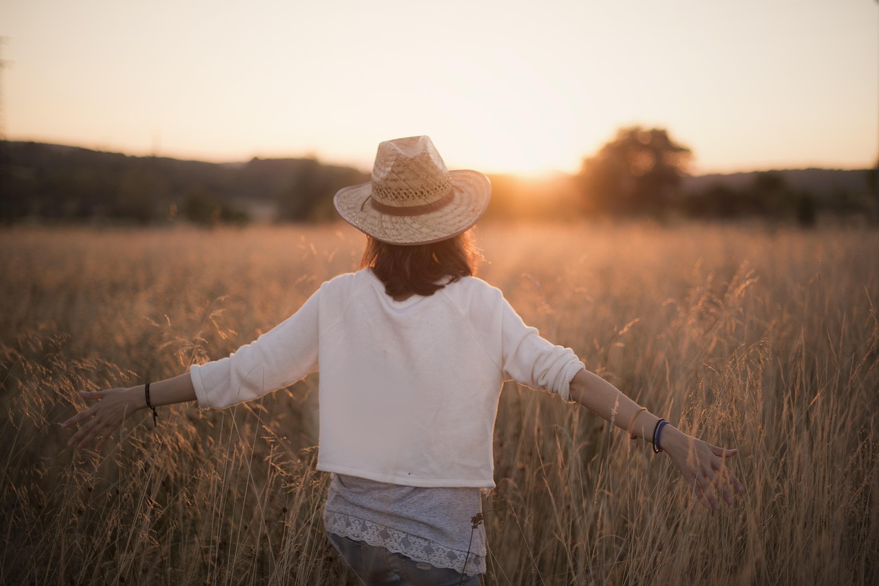 A woman wearing a straw hat and white shirt walks through a field feeling relief after emotionally detaching from someone.