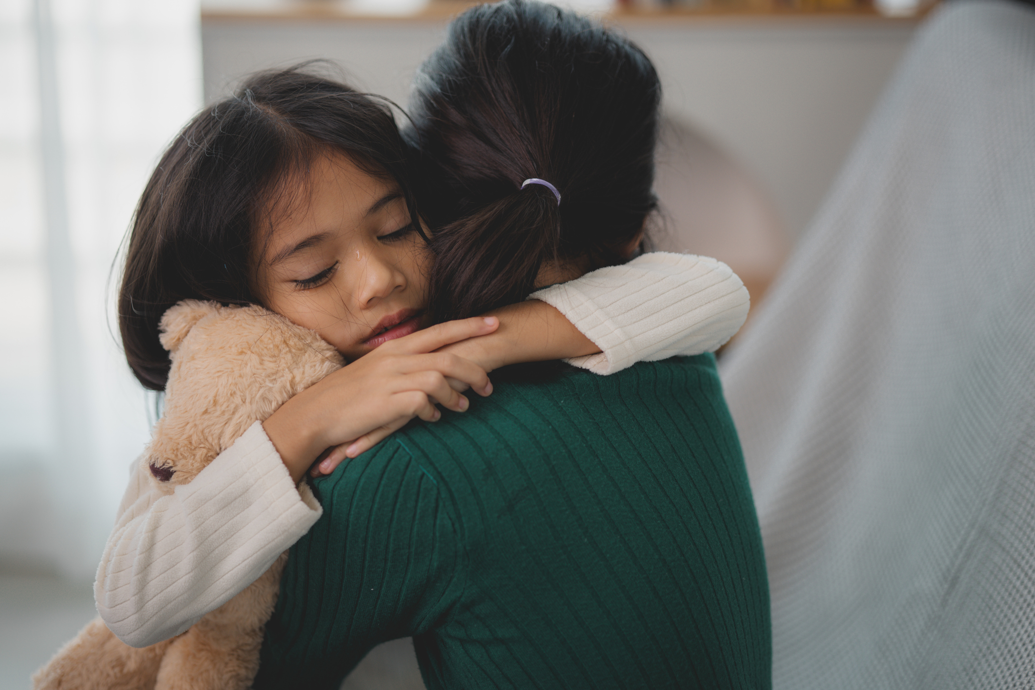 Deeply feeling kid hugging caregiver tightly with stuffed animal, representing separation anxiety and the need for emotional support.