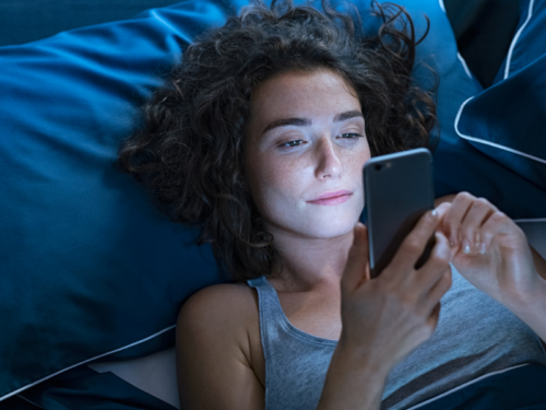 A young woman in bed on her phone looks up if main character syndrome is real.
