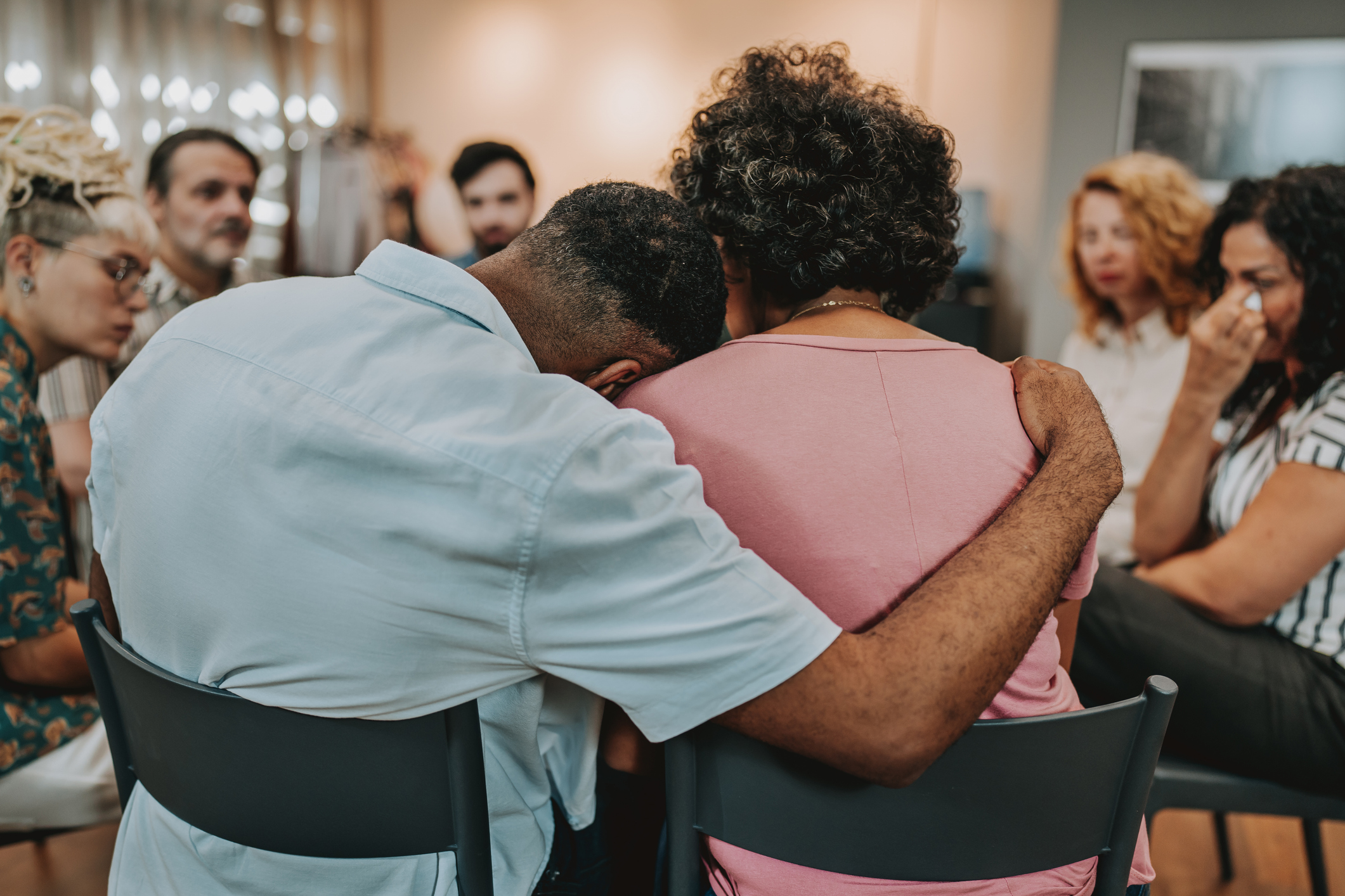 Two people supporting each other during a group therapy session as they discuss traumatic experiences.
