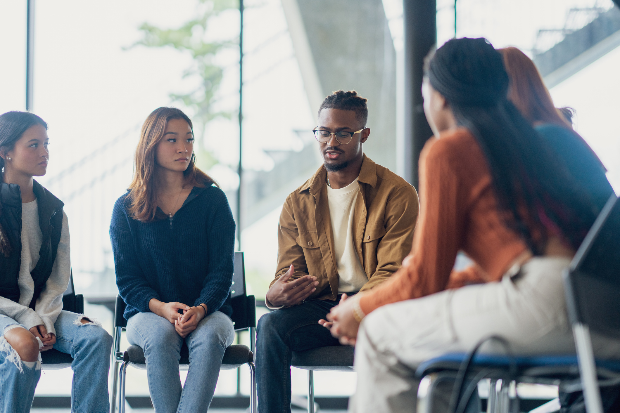 A small group of people sit together during a group therapy session sharing their struggles with the group.