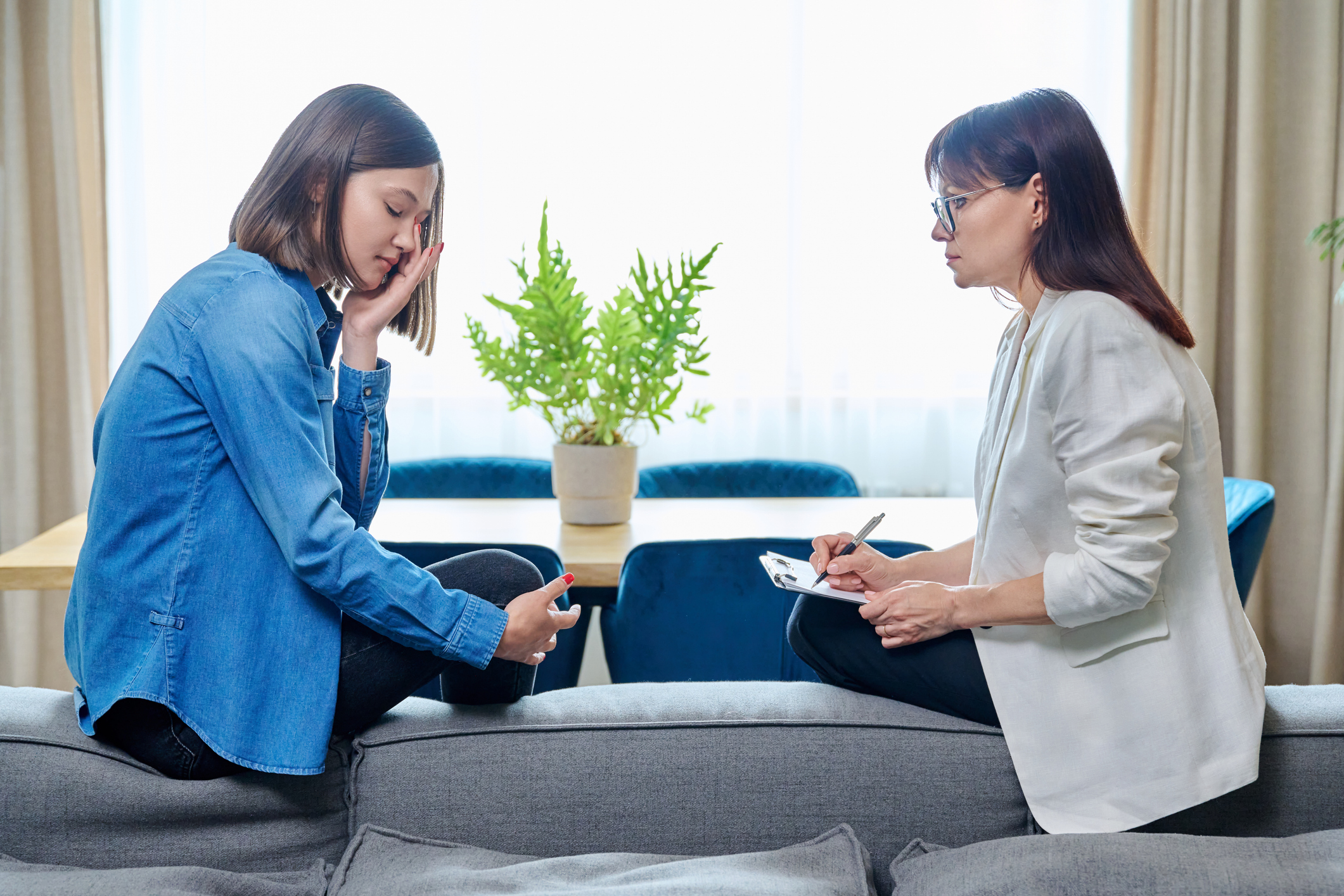 Sad crying young woman in meeting with therapist counselor sitting on couch in office talking about her abusive relationship