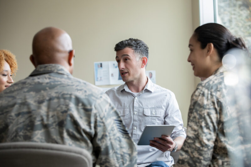 Adult male outreach support speaking to multi cultural group of soldiers during insurance education session