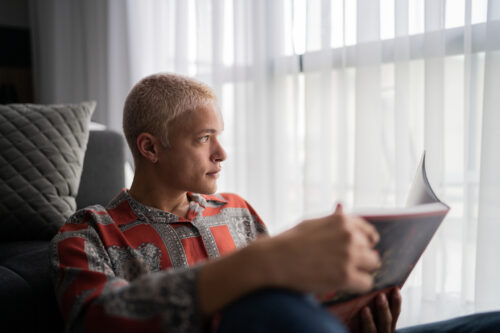 Young man contemplating while reading a book at home