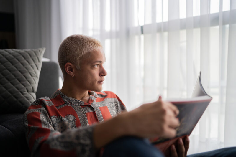 Young man contemplating while reading a book at home