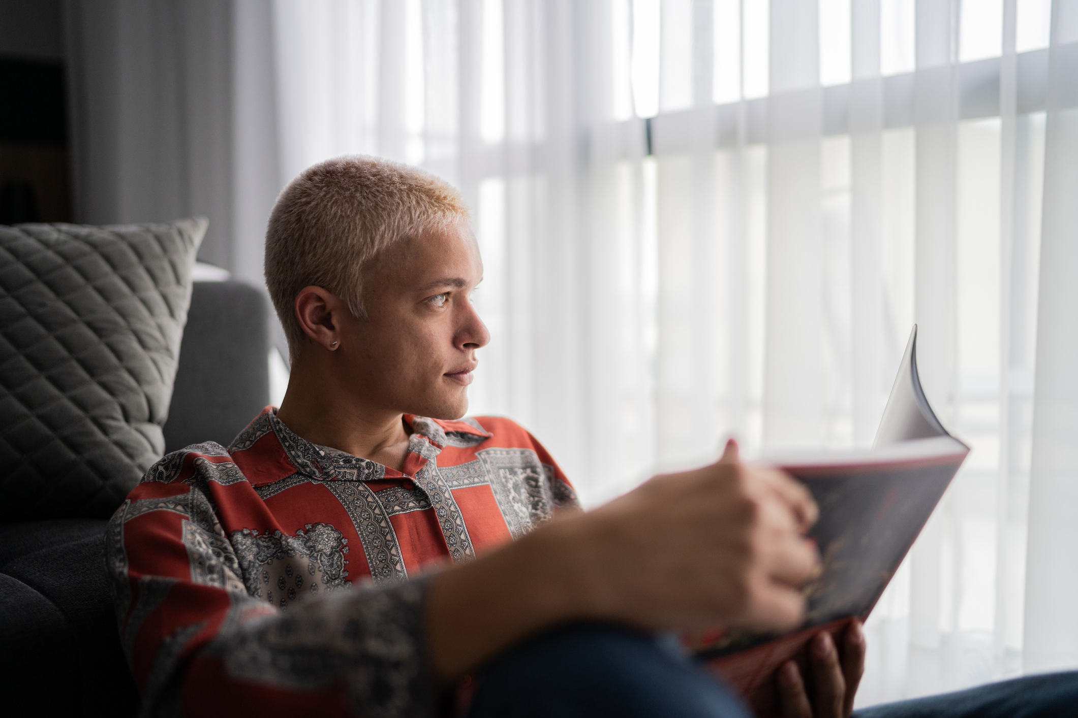 Young man contemplating while reading a book at home