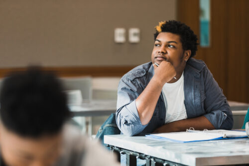The teenage boy sits distracted with his thoughts during class.