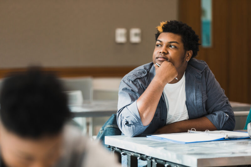 The teenage boy sits distracted with his thoughts during class.
