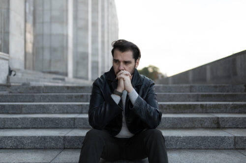 saddened and men confused why he doesn't feel like himself sits in depression on the steps of a gray building.