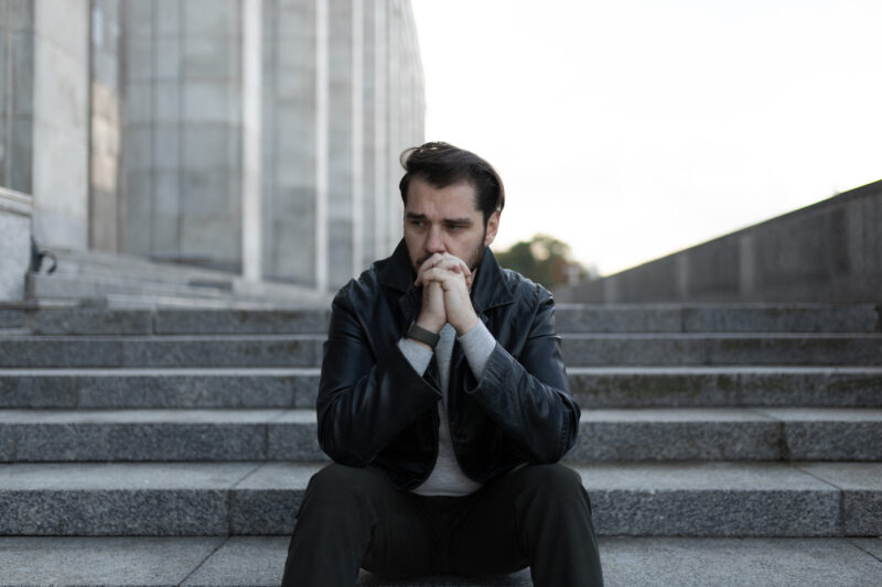 saddened and men confused why he doesn't feel like himself sits in depression on the steps of a gray building.