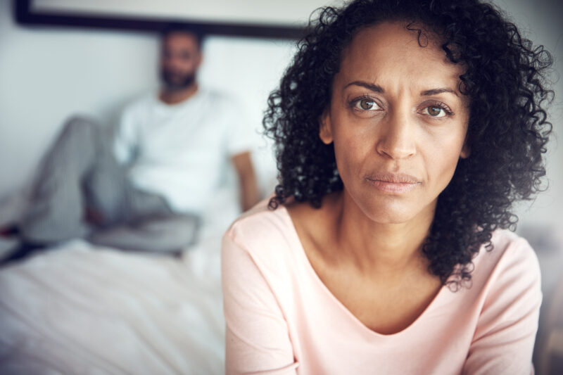 Portrait of a mature woman looking upset and having suicidal ideation, with her husband in the background